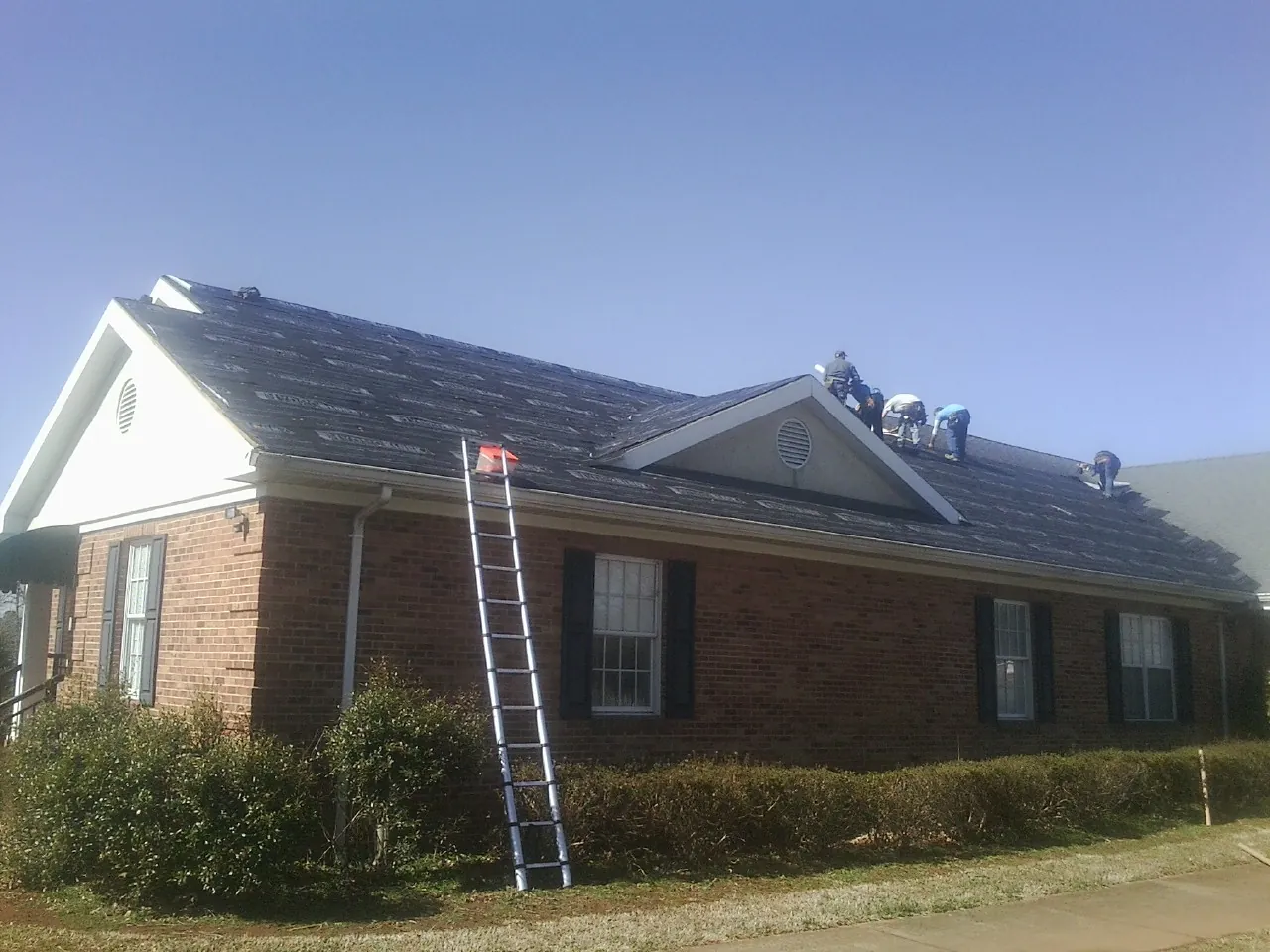 Crew tearing shingles off a brick ranch roof with a ladder set — Metal Roof Repair work by our crew in Zieglerville