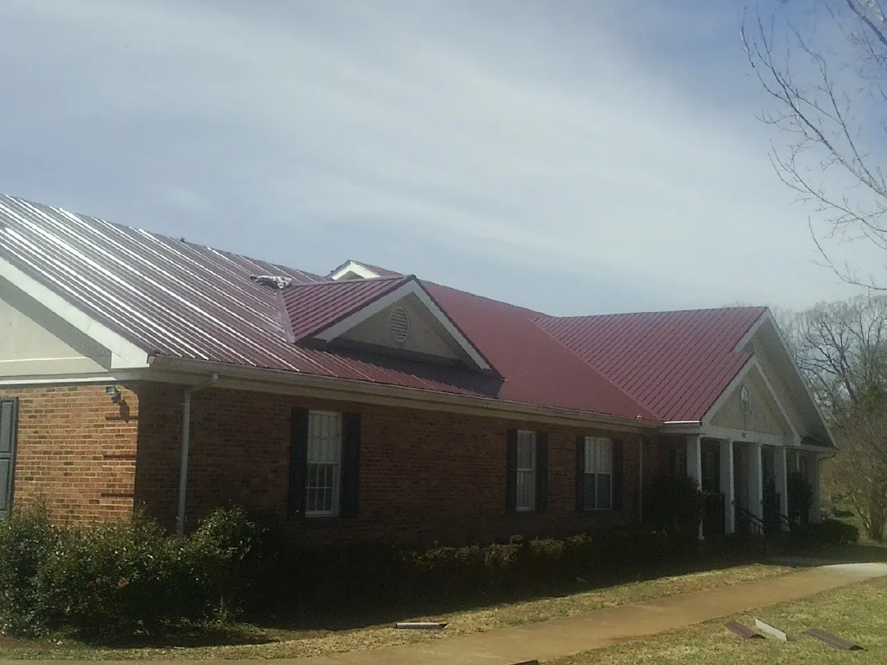 Red metal roof with gabled entries on a long brick building, from a Hail Damage Roof Repair job in Zieglerville