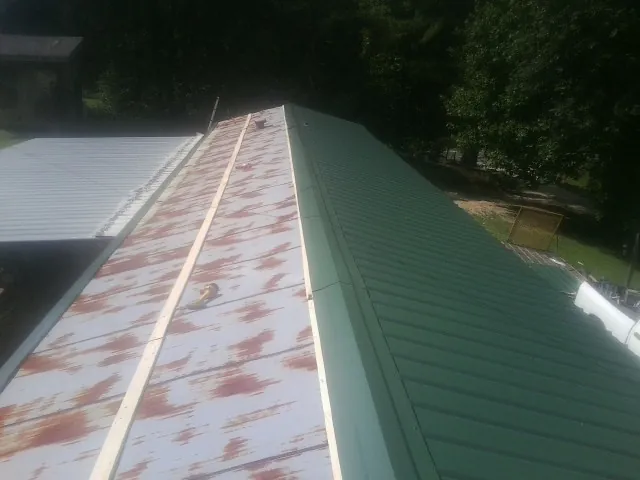 Old rusted panels beside newly installed green metal roofing — Wind Damage Roof Repair by Roofing Brothers in Zieglerville