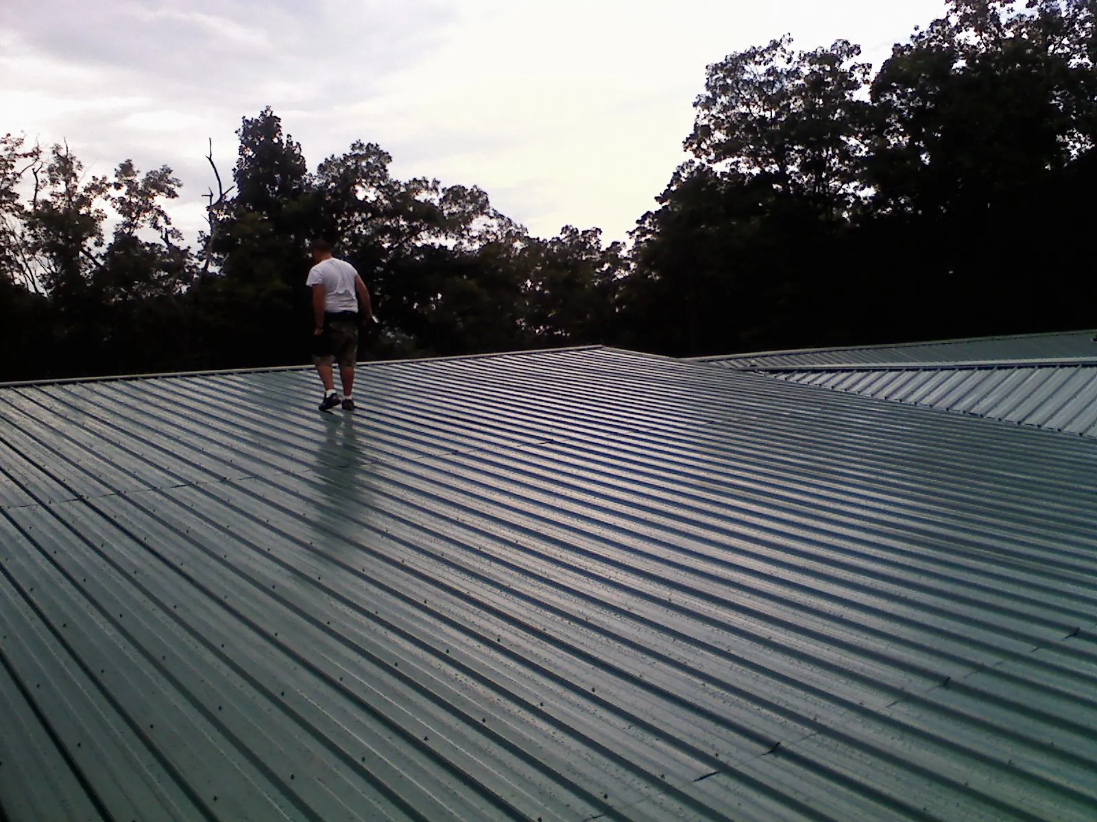 Roofer walking a wide expanse of new green metal roofing in Zieglerville
