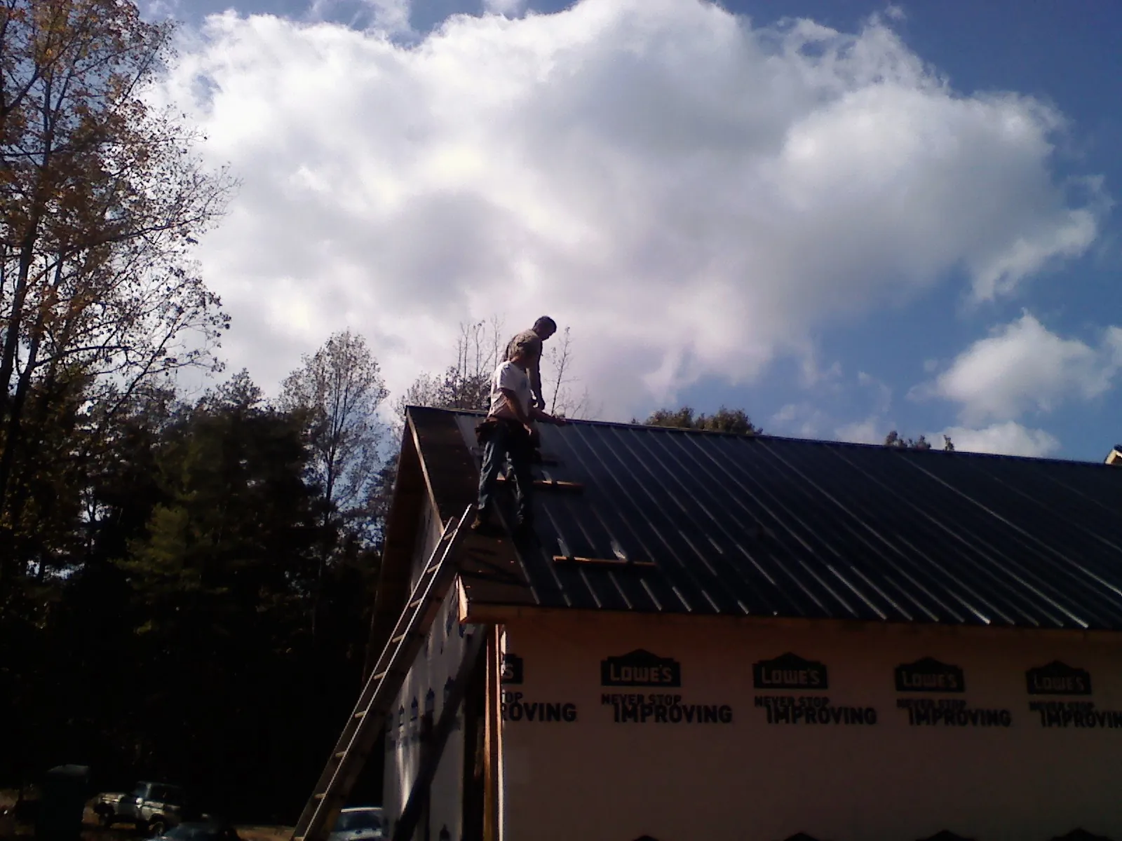 Roofer fastening dark metal panels high against a cloudy sky, from a Roof Inspection job in Zieglerville