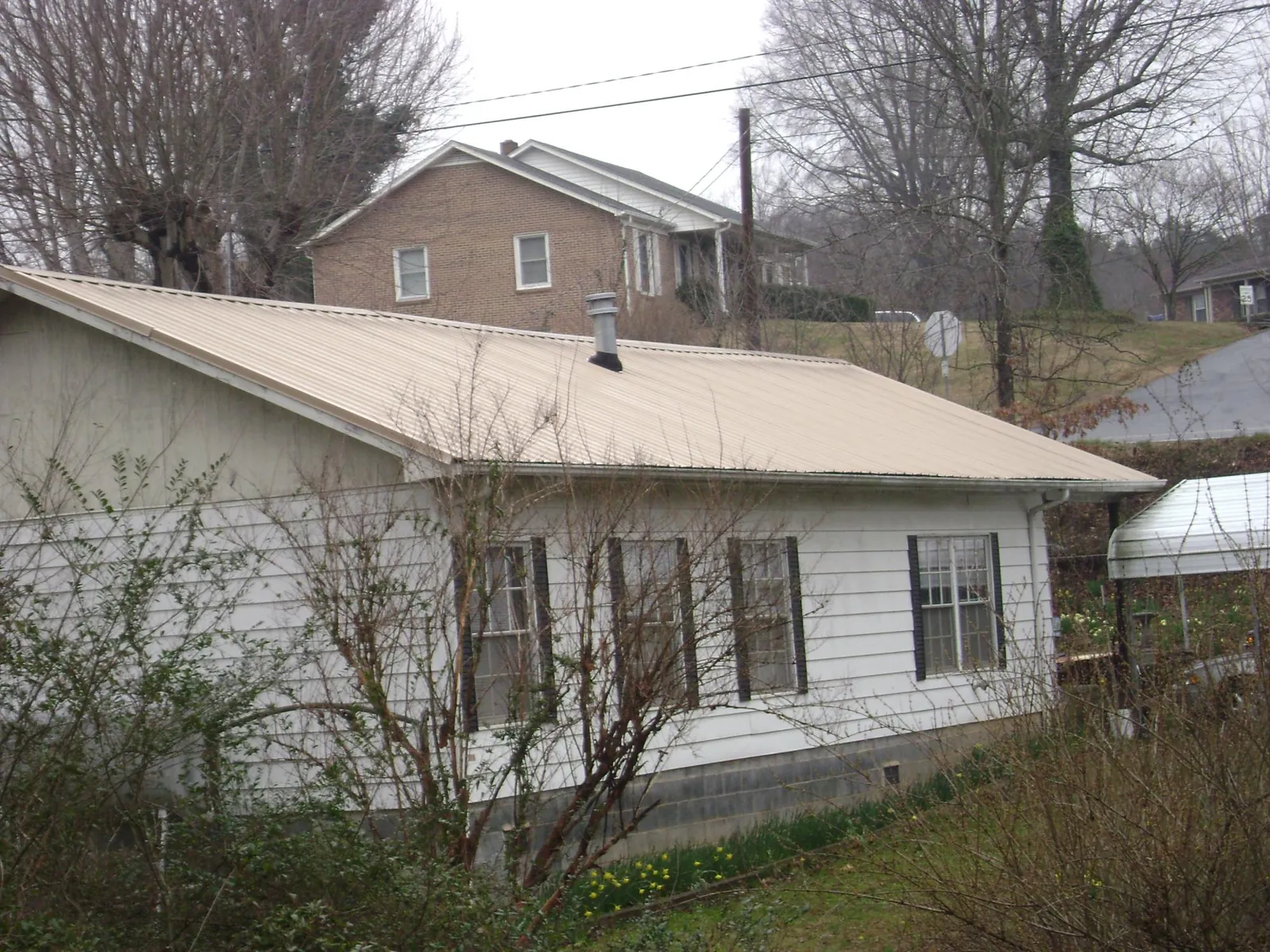 Tan metal roof on a white sided house set into a hillside — Commercial Roofing by Roofing Brothers in Zieglerville